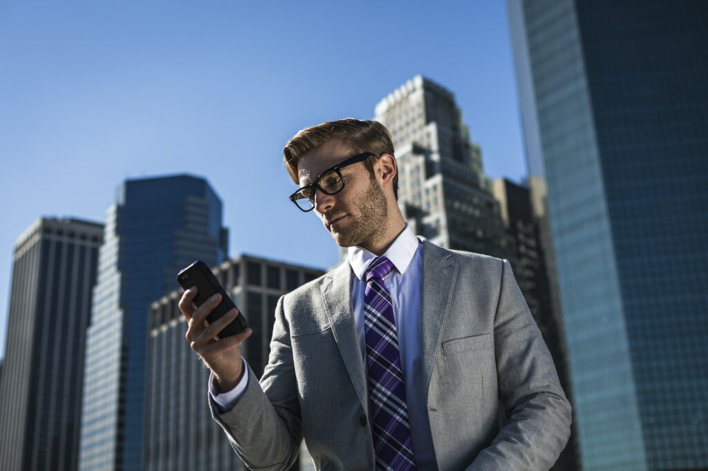 Young businessman in front of office building reading smartphone texts, New York, USA